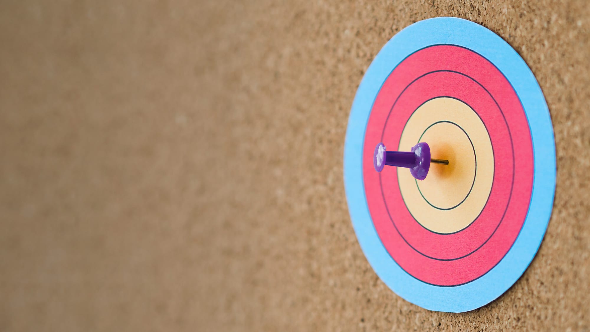 An image showing a purple pin penetrating through a colorful paper target on a wall.