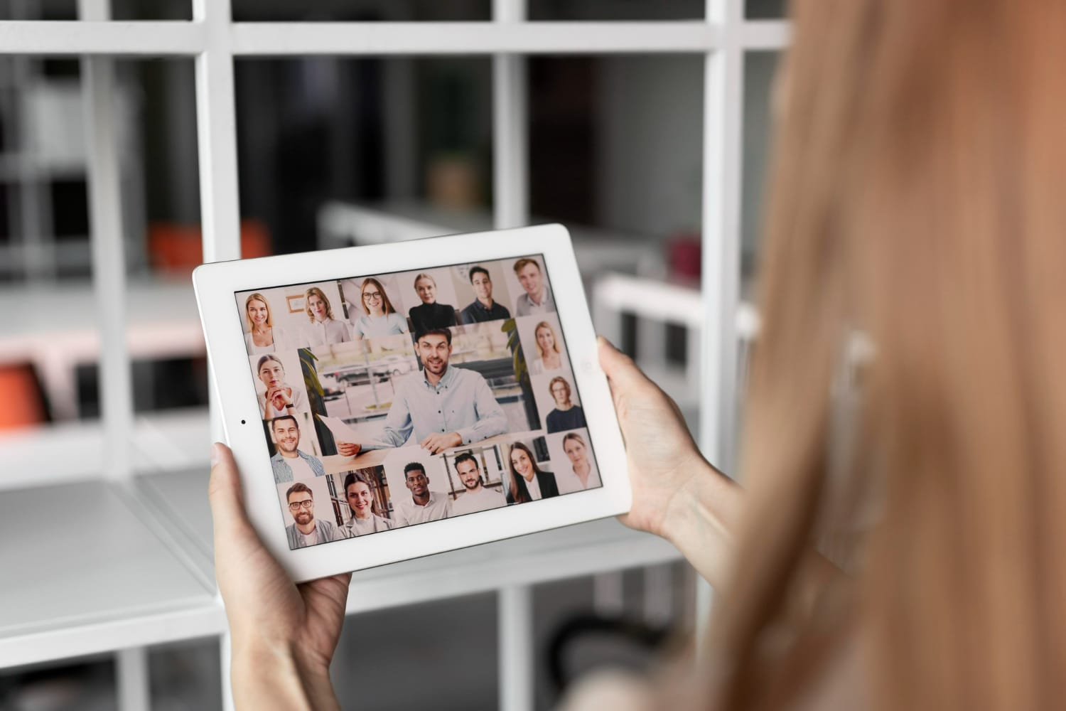 A woman holding a tablet that shows multiple people in an online meeting on a screen.