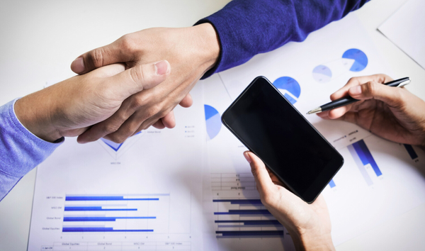 Two people shake hands in agreement over a table covered with various graphs.